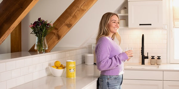 Donna che tiene in mano un bicchiere con BEAVITA Shake in cucina