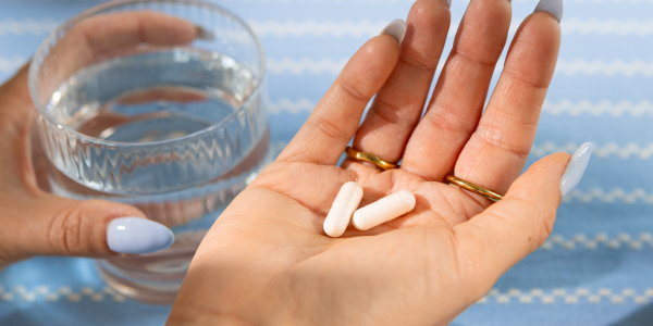 Mano con due capsule e un bicchiere d'acqua