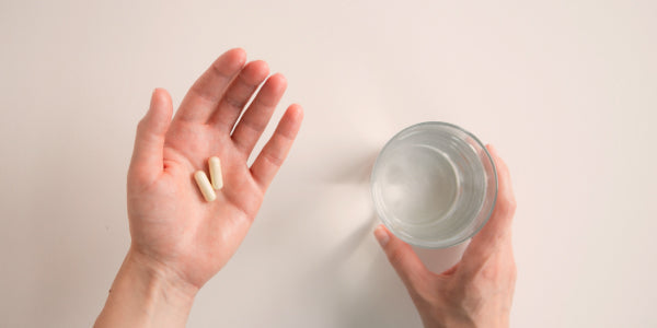 2 capsule su una mano e un bicchiere d'acqua