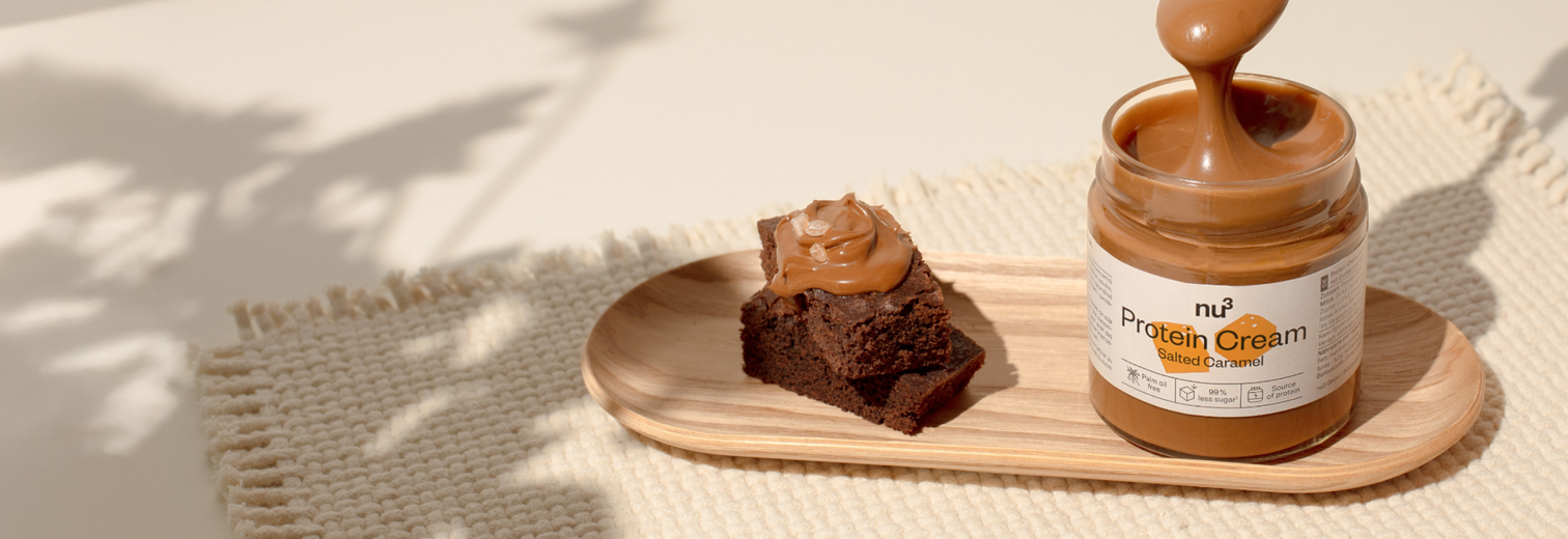 nu3 Protein Cream Salted Caramel auf einem kleinen Holzbrett, daneben ein Brownie