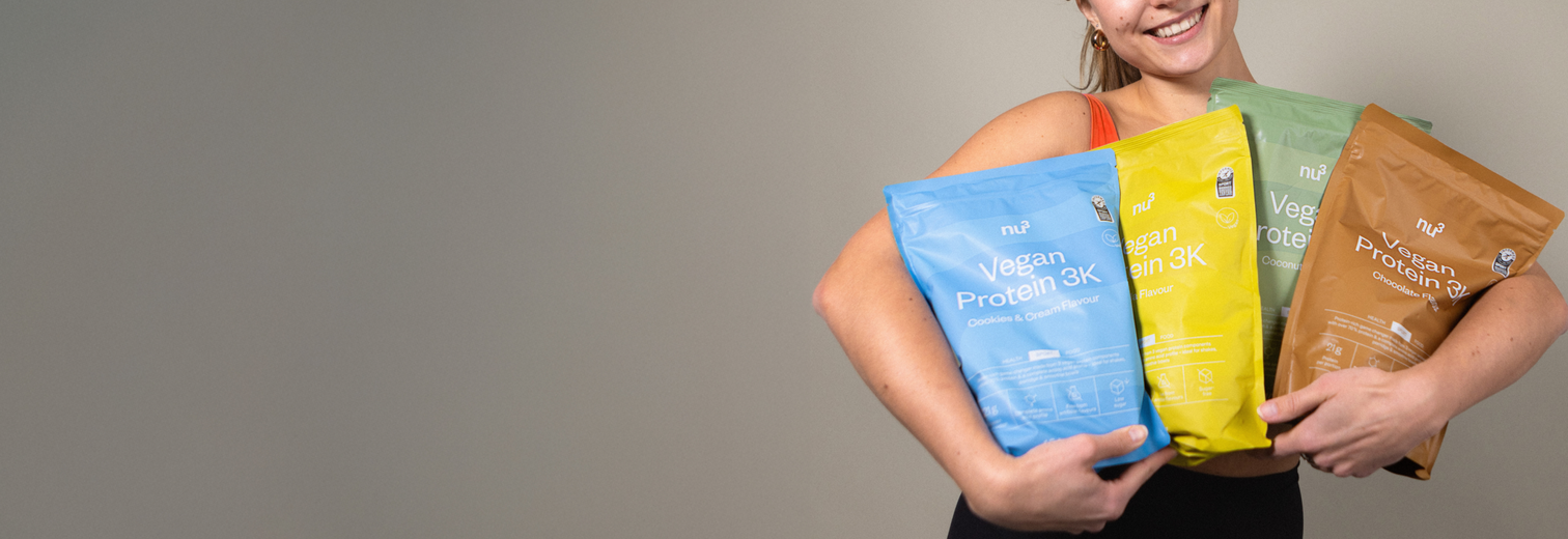 Frau trägt 4 Packungen nu3 Vegan Protein 3K