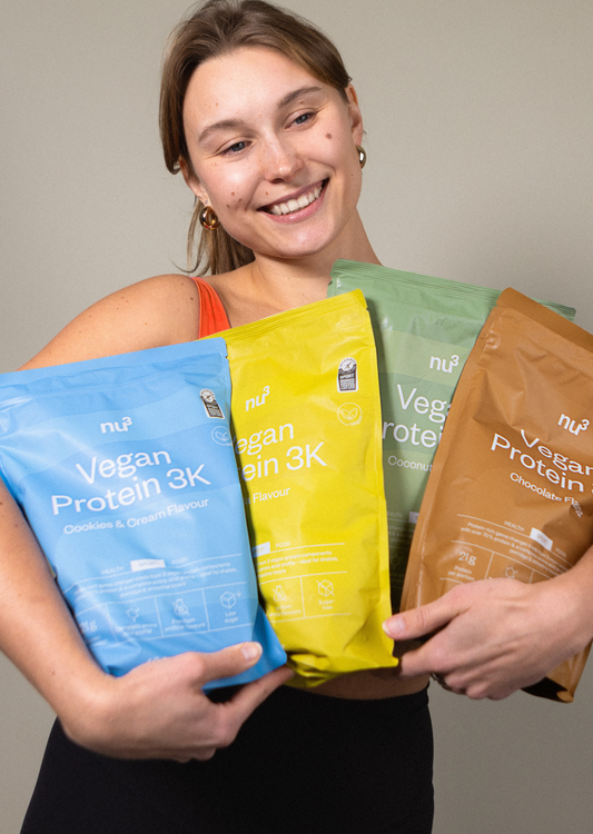 Frau trägt 4 Packungen nu3 Vegan Protein 3K