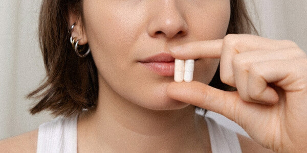 Primo piano del viso di una giovane donna dai capelli scuri che tiene due capsule tra il pollice e l'indice all'altezza della bocca